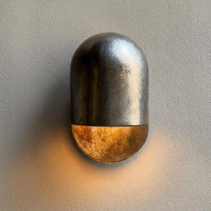 AX472 modern outdoor wall sconce in gunmetal finish, lit with a warm glow on a grey wall